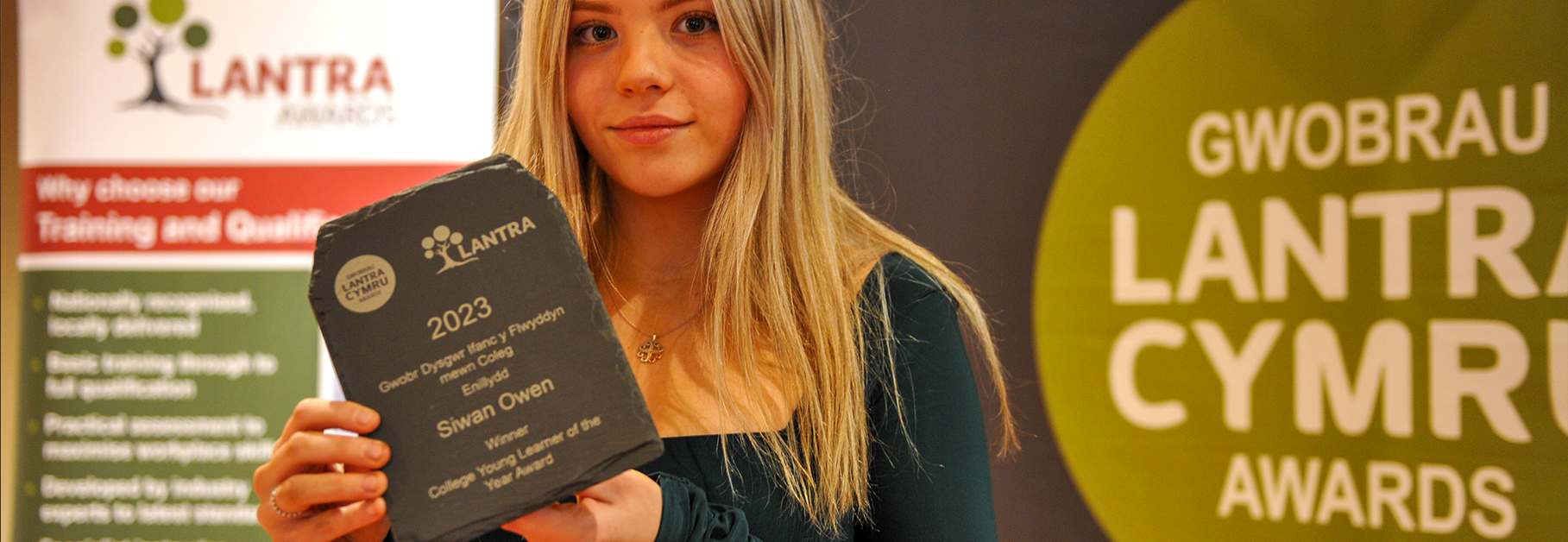 A photo of a Lantra Cymru Awards winner holding her statue in front of a branded banner